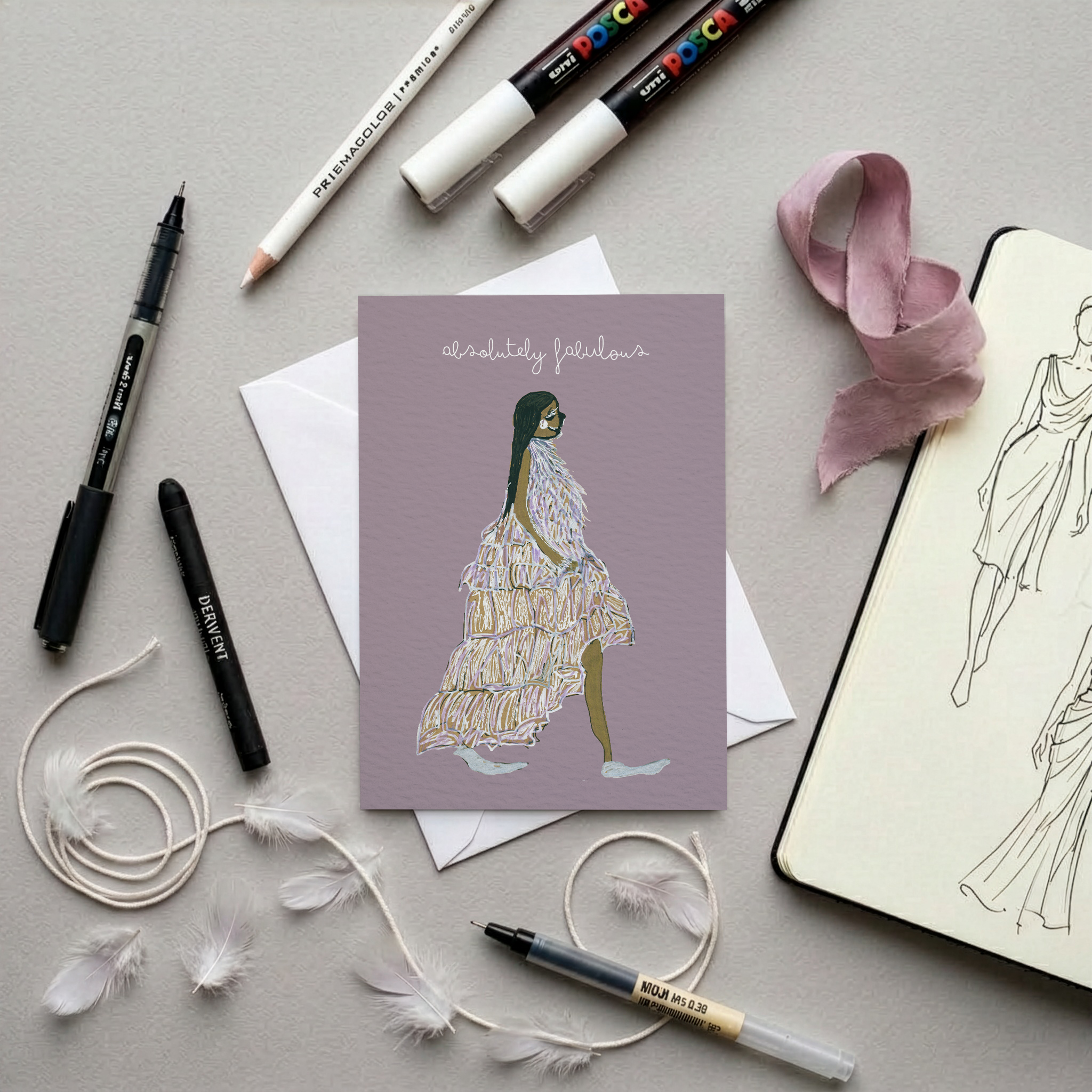 Greeting card with a stylised illustration of a woman on a purple background, surrounded by drawing tools and a notebook.