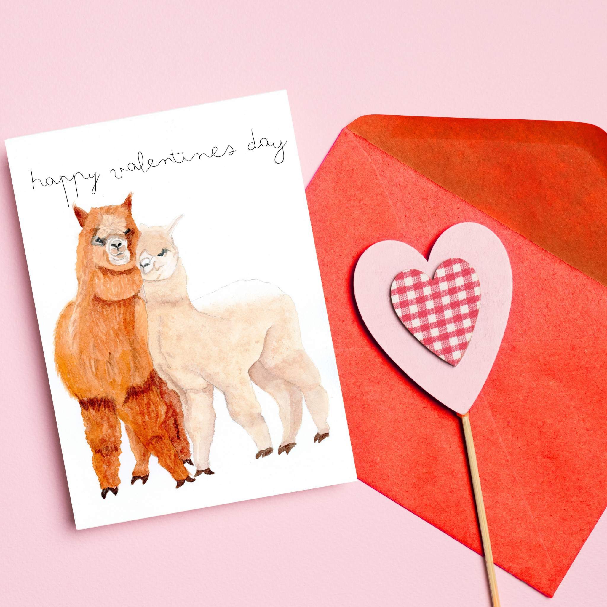 Valentine's Day card with two alpacas and a red envelope on a pink background