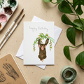 Birthday card with chimpanzee watercolour illustration on a beige surface with artist materials