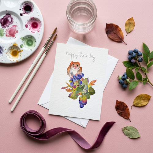 Greeting card with a mouse among berries watercolour illustration on a pink surface with art supplies and decorative elements.